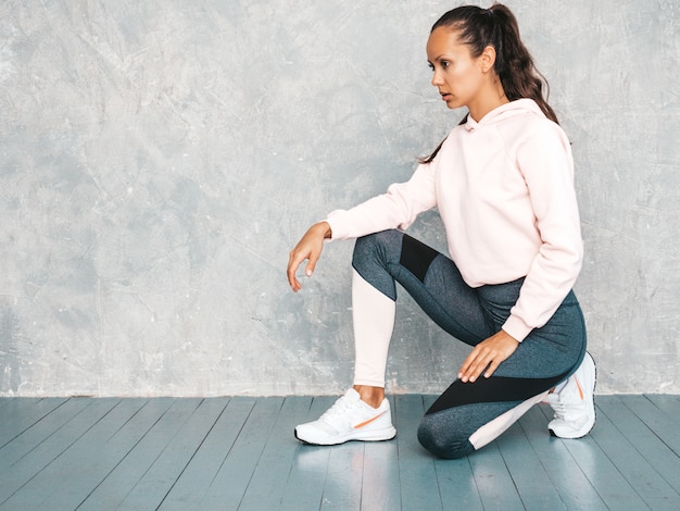 Beau Modèle Avec Un Corps Bronzé Parfait Femme Assise En Studio Près Du Mur Gris