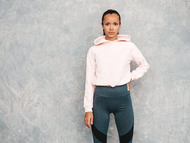 Beau modèle avec un corps bronzé parfait. Femme posant en studio près du mur gris