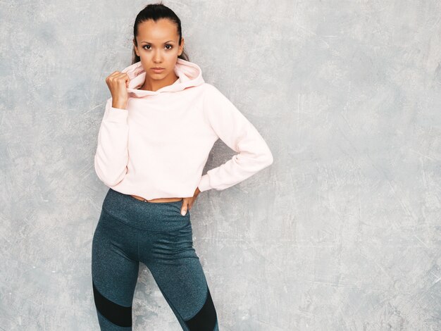 Beau modèle avec un corps bronzé parfait. Femme posant en studio près du mur gris