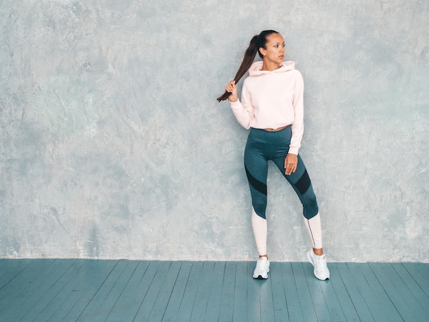 Beau modèle avec un corps bronzé parfait. Femme posant en studio près du mur gris