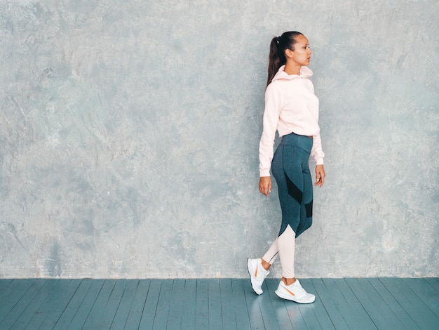 Beau modèle avec un corps bronzé parfait. Femme posant en studio près du mur gris