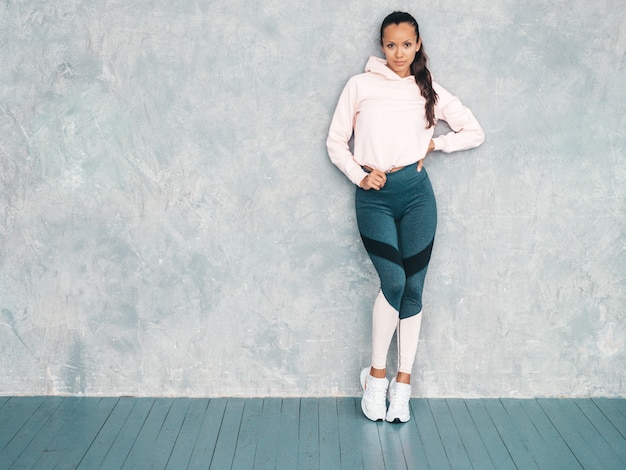 Beau Modèle Avec Un Corps Bronzé Parfait. Femme Posant En Studio Près Du Mur Gris