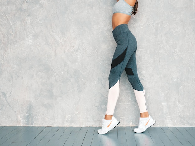 Beau Modèle Avec Un Corps Bronzé Parfait. Femme Posant En Studio Près Du Mur Gris