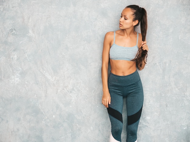 Beau modèle avec un corps bronzé parfait. Femme posant en studio près du mur gris