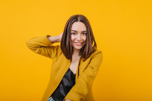 Beau modèle féminin dans des vêtements élégants jouant avec ses cheveux. Portrait de fille européenne positive en riant.