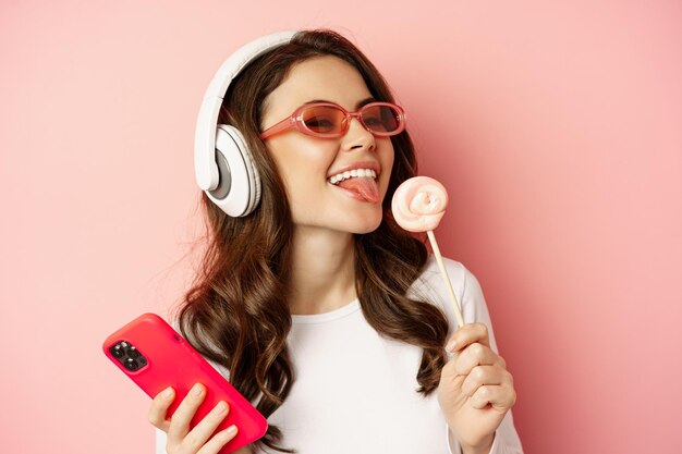 Beau modèle féminin écoutant de la musique dans des écouteurs tenant une sucette et un téléphone portable posant en chantant...