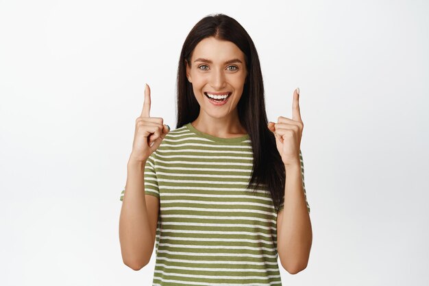 Beau modèle féminin sourit pointe les doigts vers le haut montre la bannière du logo de vente se dresse sur fond blanc