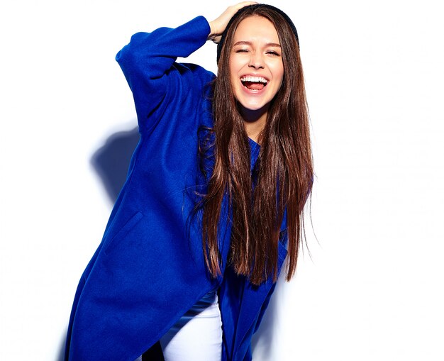 Beau modèle de femme brune hipster souriant en élégant manteau bleu isolé sur blanc. Faire un clin d'oeil