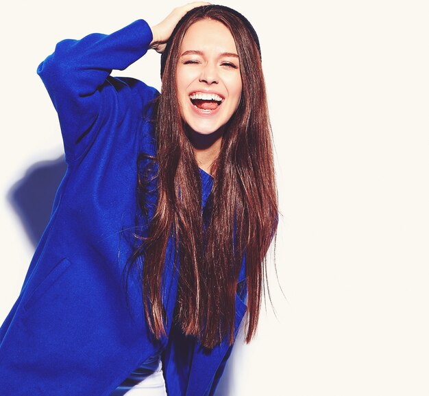 Beau modèle de femme brune hipster souriant en élégant manteau bleu isolé sur blanc. Faire un clin d'oeil