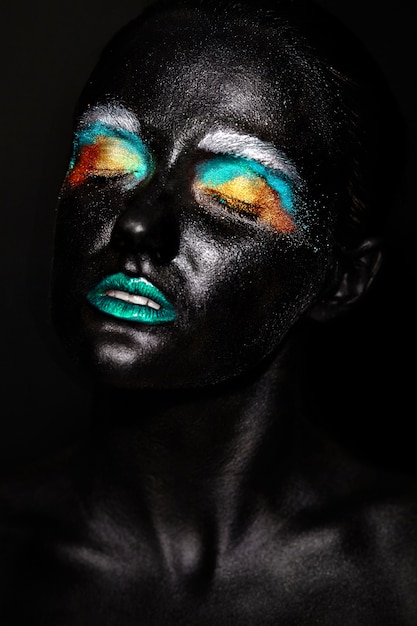 Beau modèle femme avec un masque noir inhabituel en plastique créatif maquillage coloré lumineux avec visage noir