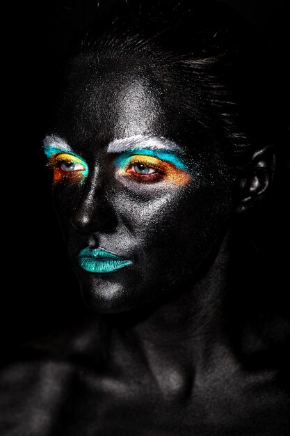 Beau modèle femme avec un masque noir inhabituel en plastique créatif maquillage coloré lumineux avec visage noir