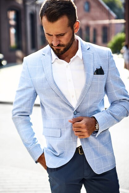 Photo gratuite beau modèle d'homme d'affaires de mode vêtu d'un élégant costume bleu posant sur la rue