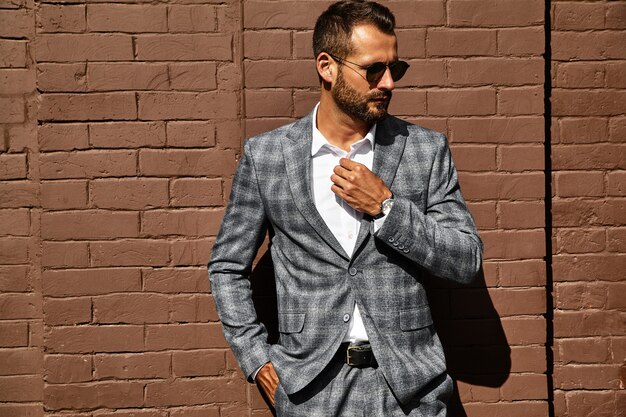 beau modèle homme d'affaires de mode vêtu d'un élégant costume à carreaux posant près du mur de briques dans la rue