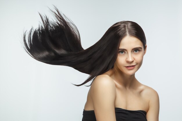 Beau modèle avec de longs cheveux bruns lisses et volants isolés sur fond de studio blanc.