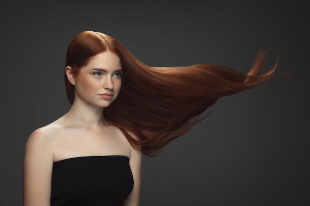 Beau modèle avec de longs cheveux roux lisses et volants isolés sur fond sombre