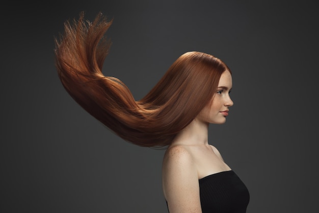 Beau modèle avec de longs cheveux roux lisses et volants isolés sur fond sombre