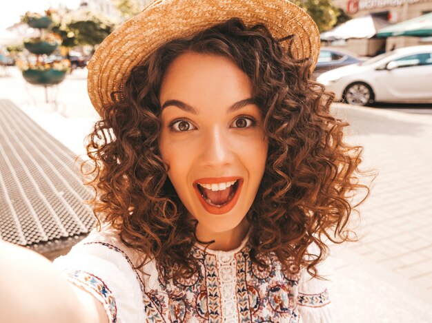 Beau modèle souriant avec une coiffure de boucles afro habillée en robe blanche d'été hipster.