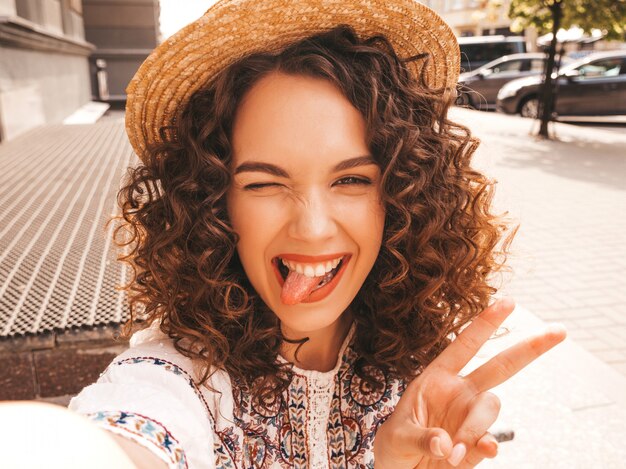 Beau modèle souriant avec une coiffure de boucles afro habillée en robe blanche d'été hipster.