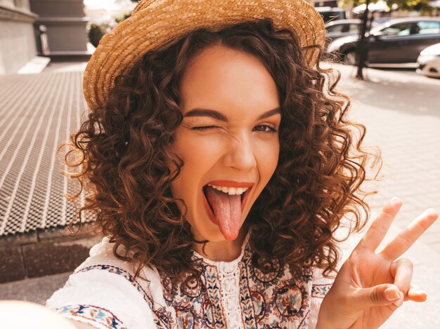 Beau modèle souriant avec une coiffure de boucles afro habillée en robe blanche d'été hipster.