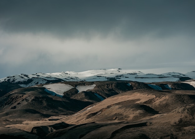 Beau paysage naturel avec des collines enneigées et un ciel gris foncé