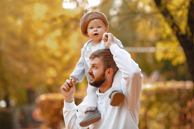 Beau père dans un pull gris, jouant avec une petite fille dans un parc en automne