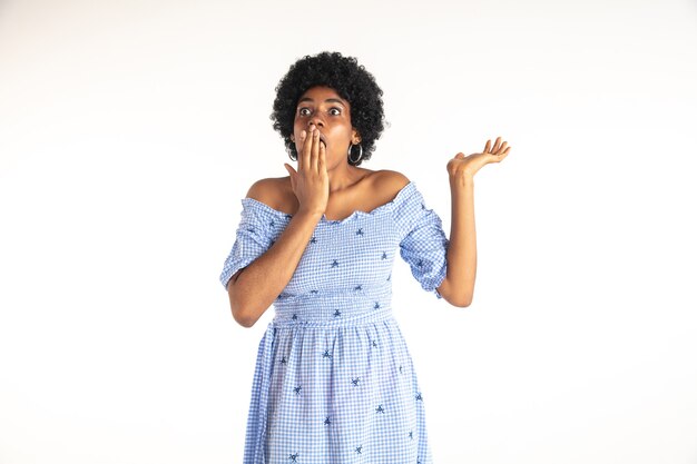 Beau portrait de demi-longueur féminin sur fond de studio blanc. Jeune femme afro-américaine émotionnelle en robe bleue.