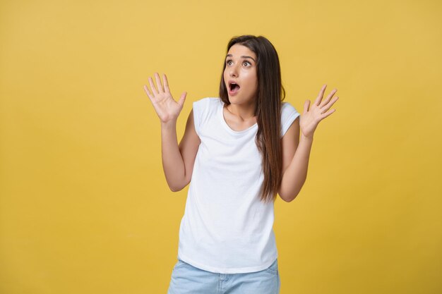 Beau portrait féminin demi-longueur isolé sur fond de studio jaune La jeune femme émotionnelle souriante et surprise debout et regardant la caméra Le concept d'expression faciale des émotions humaines