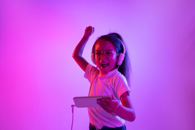 Beau portrait féminin isolé sur fond violet en néon. Fille émotionnelle à lunettes. Émotions humaines, concept d'expression faciale. Danser, écouter de la musique, jouer et gagner.