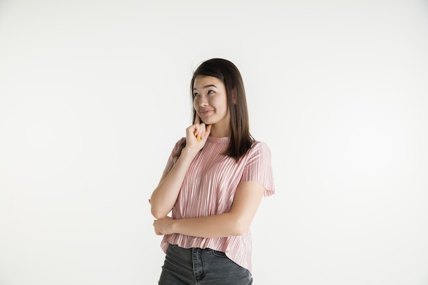 Beau portrait de femme demi-longueur isolé sur fond de studio blanc. Jeune femme émotionnelle dans des vêtements décontractés. Émotions humaines, concept d'expression faciale. Pense ou rêve, semble pensif.