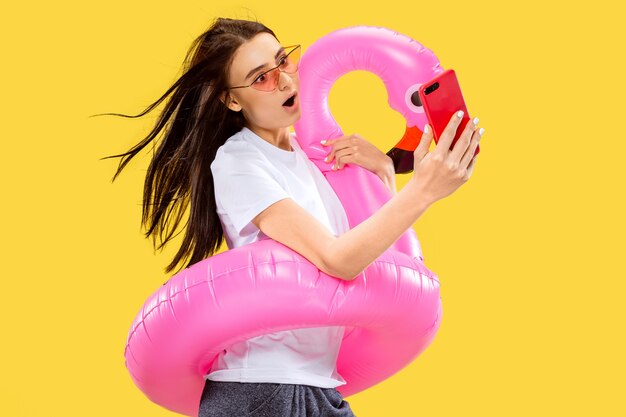 Beau portrait de femme demi-longueur isolé sur mur jaune. Jeune femme souriante à lunettes de soleil rouges faisant selfie. Expression faciale, été, week-end, concept de villégiature. Couleurs à la mode.