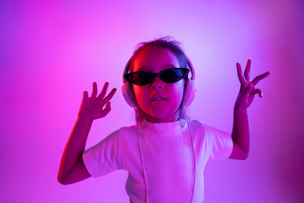 Beau portrait de femme demi-longueur isolé sur mur violet en néon. Jeune adolescente émotionnelle à lunettes de soleil. Émotions humaines, concept d'expression faciale. Couleurs à la mode. Danser, sourire.