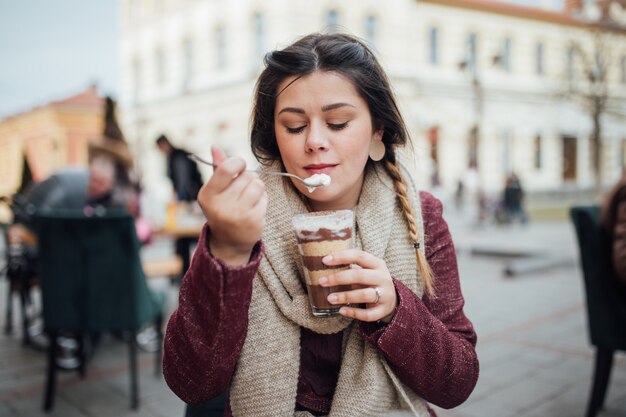 Beau portrait d'une jolie fille mangeant un dessert au chocolat de la tasse dans le café de la rue
