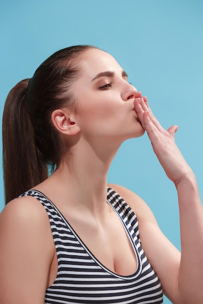 Beau portrait de trois quarts féminin. isolé sur fond de studio bleu. La belle jeune femme émotive est debout. Les émotions humaines, le concept d'expression faciale. Vue de profil. Couleurs tendance