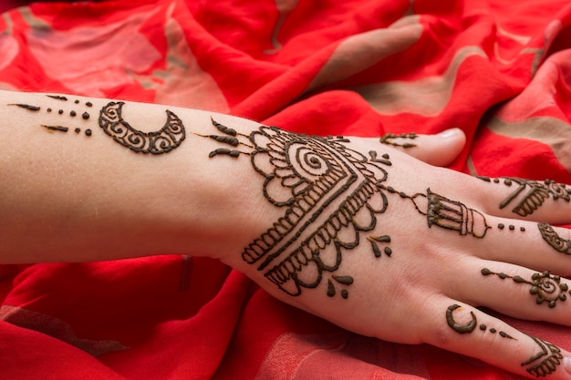 Photo gratuite beau tatouage de mehndi sur la main de la femme placée sur du textile rouge