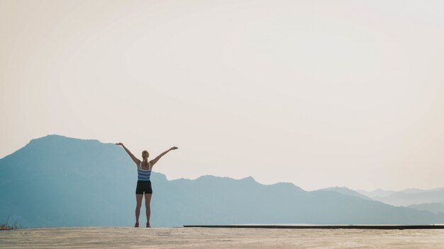 Beau tir d'une femme debout sur le sol avec les silhouettes de collines en arrière-plan