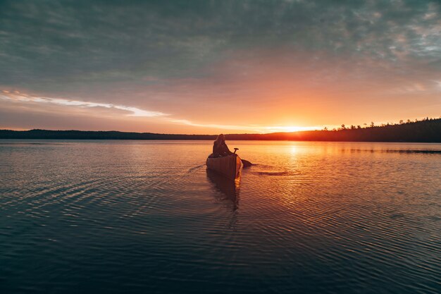 Beau tir lointain d'une femme en kayak au milieu d'un lac pendant le coucher du soleil