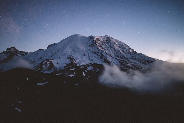 Beau tir d'une montagne enneigée entourée de brume naturelle avec un ciel étoilé incroyable