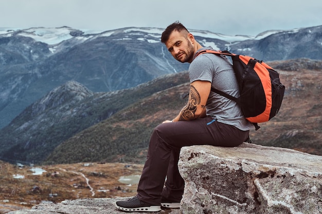 Un beau touriste barbu est assis sur un rocher en arrière-plan d'un magnifique paysage de montagne en Norvège.