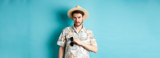 Beau touriste en chemise hawaïenne et chapeau d'été mettre des lunettes de soleil dans la poche en vacances standin