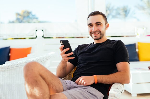 Beau touriste lire et envoyer des SMS sur téléphone mobile pendant la détente au café avec terrasse.