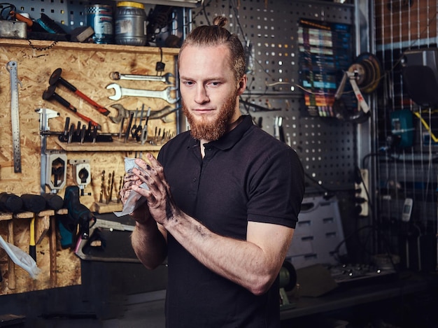 Un beau travailleur rousse élégant, nettoyant ses mains sales après avoir réparé le travail dans un atelier.