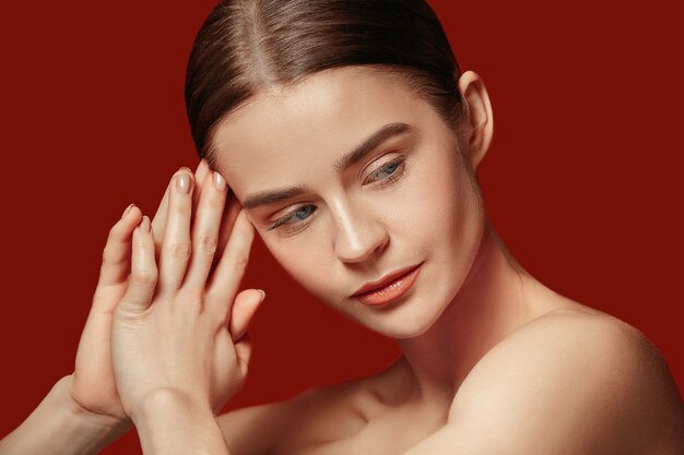 Un beau visage féminin. Peau parfaite et propre de jeune femme caucasienne sur fond de studio rouge.