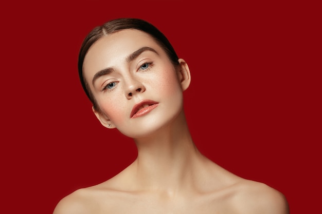 Un beau visage féminin. Peau parfaite et propre de jeune femme caucasienne sur fond de studio rouge.