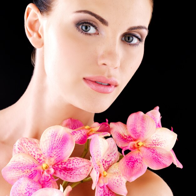 Beau visage d'une femme adulte avec une peau saine et des fleurs roses sur le corps - studio