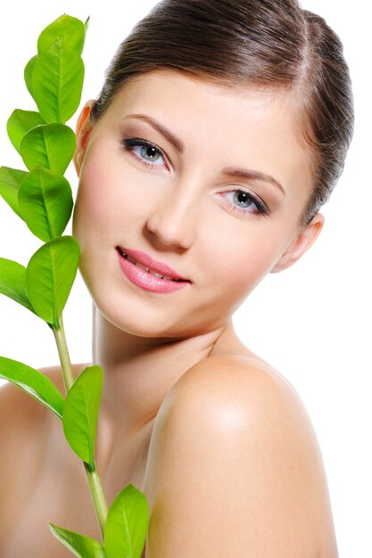 Beau visage de femme souriant avec une peau propre et saine et une plante près de son corps