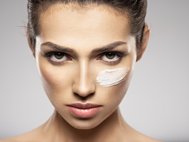 Photo gratuite beau visage de jeune femme avec frottis de crème cosmétique sur le visage près des yeux. concept de soins de la peau. concept de traitement de beauté.