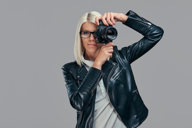 Beauté Blonde Intelligente Femme Photographe Dans Un Chemisier Blanc Et Une Veste En Cuir Noir Prenant Une Photo Dans Un Studio. Isolé Sur Un Fond Gris.