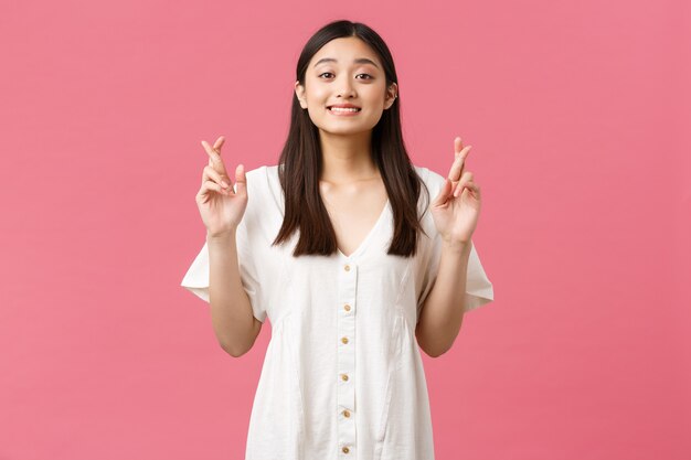 Beauté, émotions des gens et concept de loisirs d'été. Fille asiatique kawaii rêveuse pleine d'espoir en robe blanche faisant un vœu, croisant les doigts bonne chance et regardant la caméra, anticipant de bonnes nouvelles.