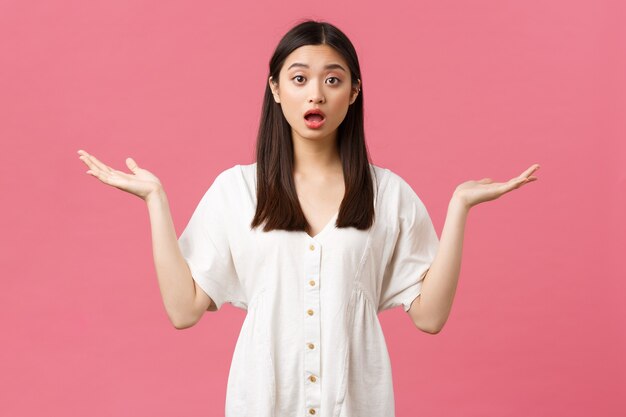 Beauté, émotions des gens et concept de loisirs d'été. Fille asiatique troublée et confuse en robe blanche debout sans aucune idée, a besoin d'aide, haussant les mains les mains écartées sur le côté et regard nerveux