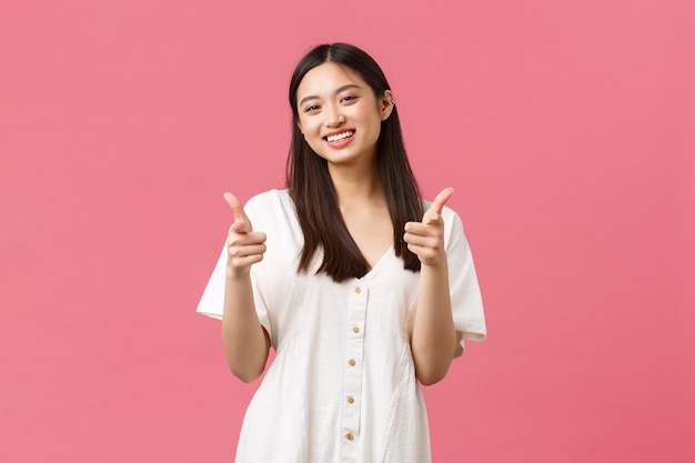 Beauté, émotions des gens et concept de loisirs et de vacances d'été. Joyeuse fille coréenne idiote en robe blanche, montrant le pouce levé et souriant, souriante contente, satisfaite du produit, le recommande